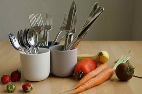 © Vesch NI | Auf einem Tisch steht Besteck in eine Tasse gestellt, daneben liegt Gemüse