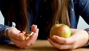 © Vesch NI | Ein junger Mensch mit Süssigkeiten in der einen Hand und in der anderen einen Apfel